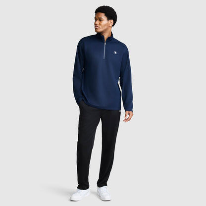 A man stands against a plain light gray background wearing the Champion Sport Long Sleeve 1/4 Zip Mockneck with C Logo, paired with black pants and white sneakers.