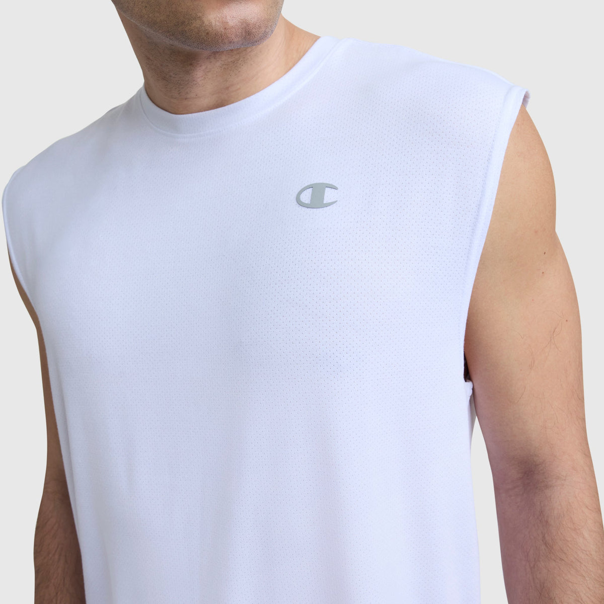 Close-up of a man in a sleeveless white Champion Sport Crewneck Muscle Tee, Script Logo, with a small script logo on the left chest. His face is partially out of the frame against a plain light gray background.