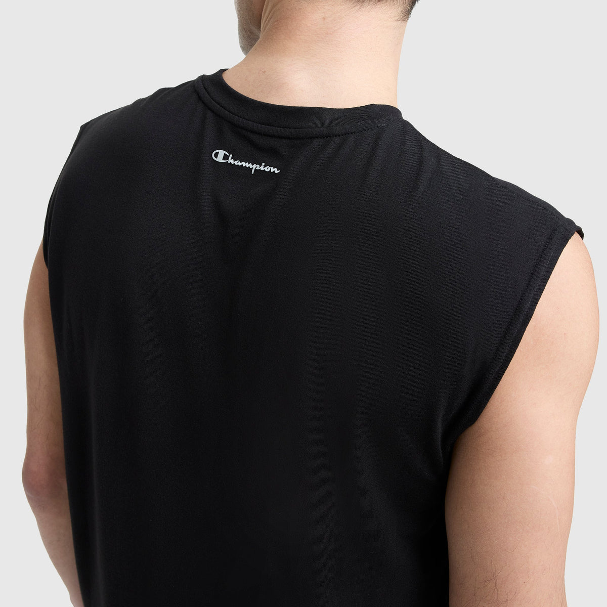 A person is seen from behind wearing a sleeveless black Champion Sport Crewneck Muscle Tee, Script Logo, with the brand’s logo near the neckline, set against a light gray background.