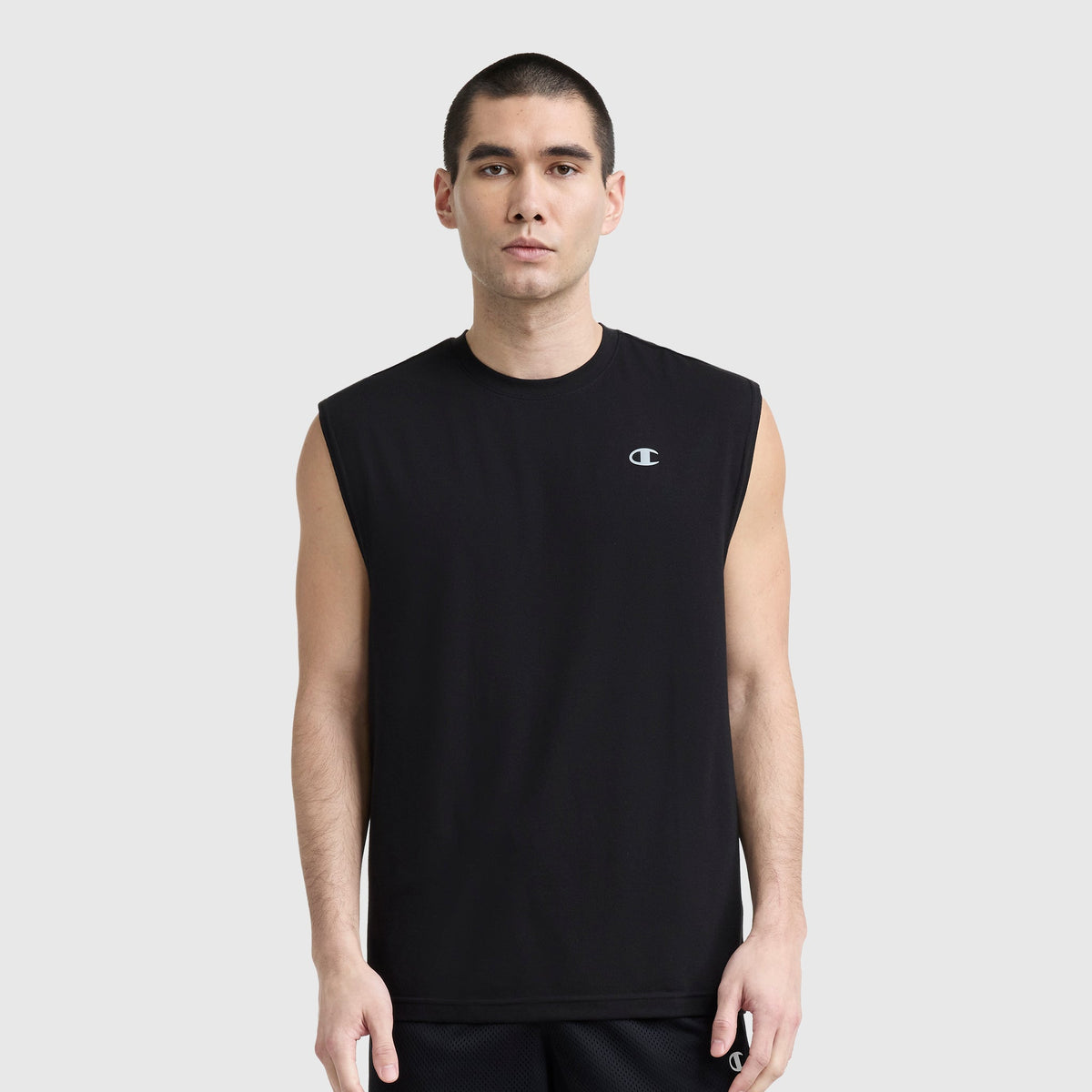 A man with short dark hair wears a black Champion Sport Crewneck Muscle Tee with script logo and black shorts, standing against a plain light gray background.