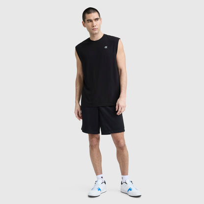 A man stands against a light gray background wearing a Champion Sport Crewneck Muscle Tee with Script Logo, black shorts, white socks, and white sneakers, looking to the side in a relaxed pose.