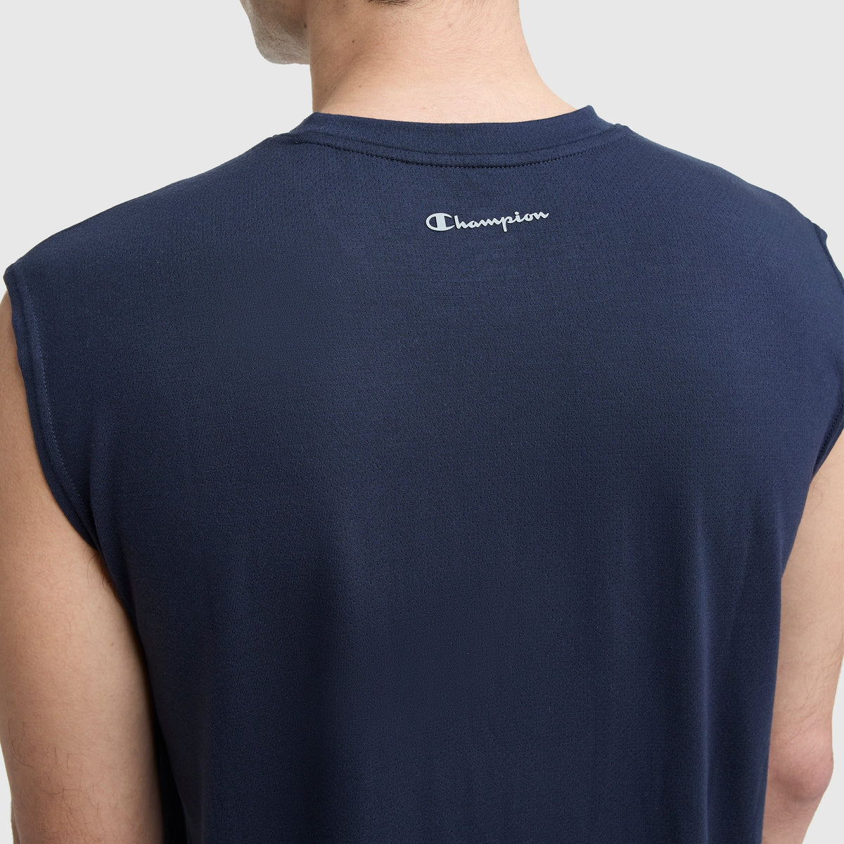 A person wearing a sleeveless navy blue Champion Sport Crewneck Muscle Tee, Script Logo, shown from the back. The Champion name and logo appear near the neckline.
