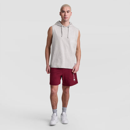 A man with short blond hair wears a Champion Sleeveless Hoodie with an embroidered C logo, maroon shorts featuring a vertical white logo, gray socks, and white sneakers, standing against a plain light gray background.