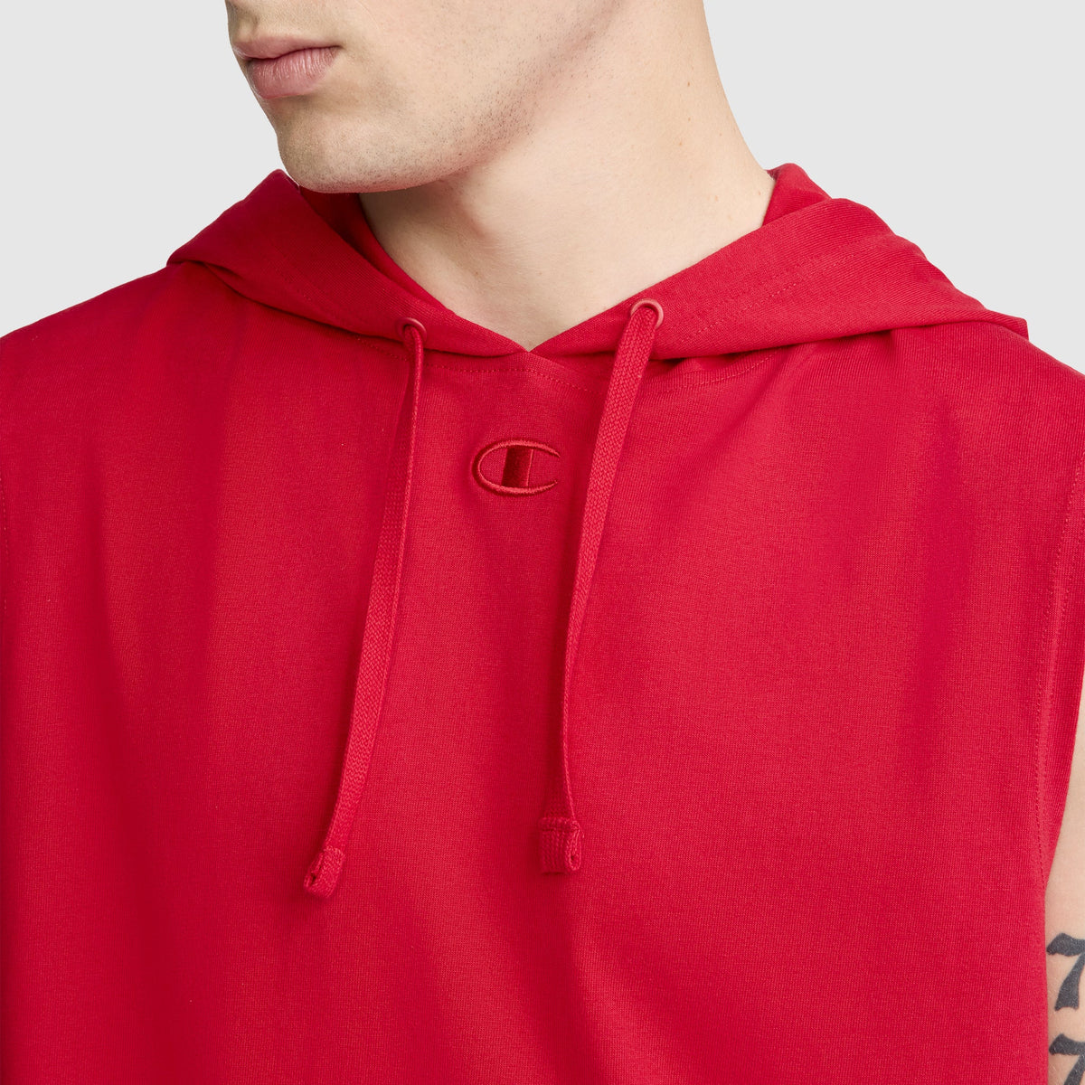 A person wearing the Champion Jersey Sleeveless Hoodie, featuring the C Logo on the chest and adjustable drawstrings. Made from soft ring-spun cotton, this red hoodie reveals only their lower face, neck, and upper torso.
