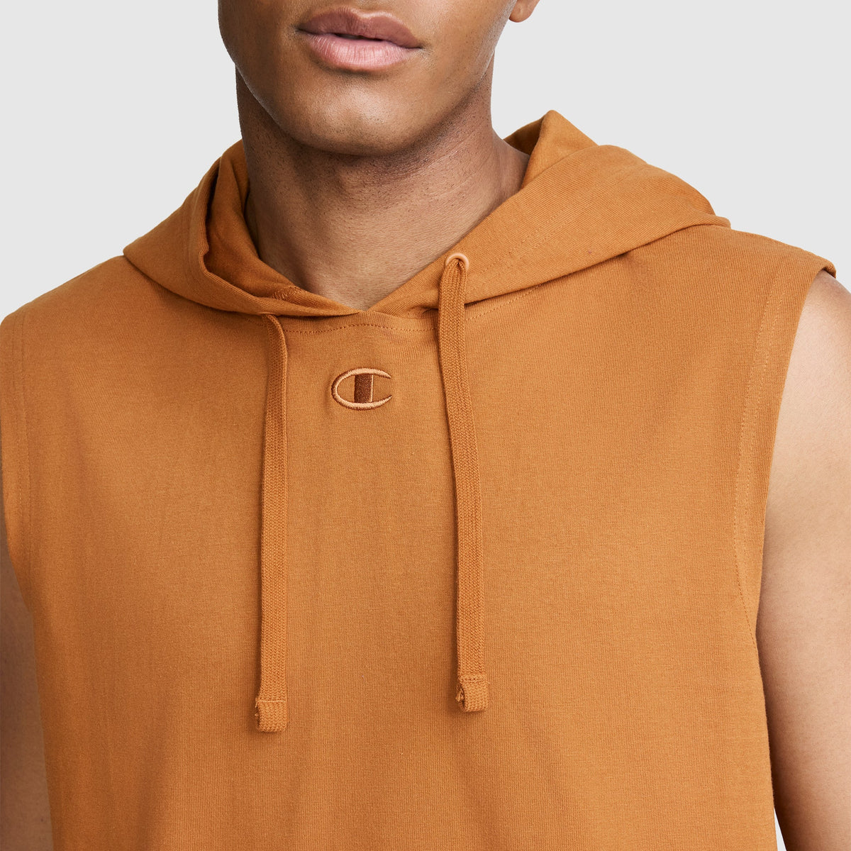 A person wearing the Champion Jersey Sleeveless Hoodie, C Logo in orange, featuring drawstrings and a small embroidered C logo near the neckline, crafted from soft ring-spun cotton, shown from the shoulders up against a plain background.