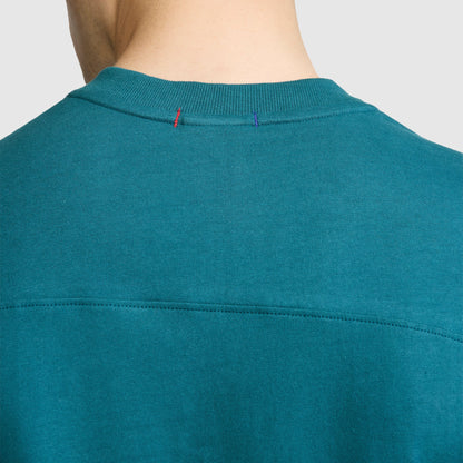 Close-up of the back neckline of a teal Champion Short Sleeve Boxy T-Shirt with an embroidered script logo, crafted from soft ring-spun cotton. The collar features red and blue stitches, and the image is cropped to show only the neck and upper back of a person.