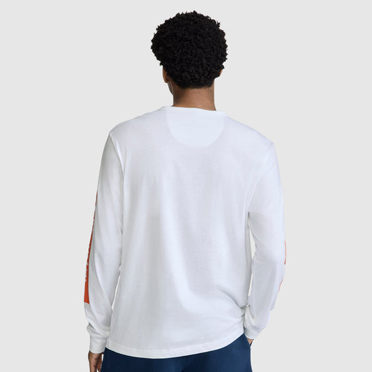 A person with short curly hair is wearing the Champion Medallion Long Sleeve Graphic T-Shirt and dark pants, standing with their back to the camera against a plain light gray background.