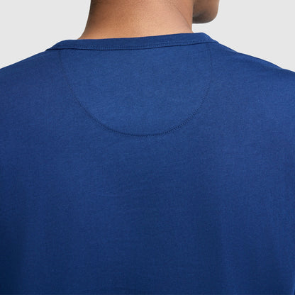 Close-up of the back of a person wearing a Champion Medallion Long Sleeve Graphic T-Shirt, showing the upper portion of the shirt and part of the person's neck against a light background.