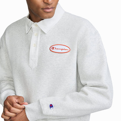 A person is wearing the Champion Fleece Rugby, a men’s rugby shirt in light gray featuring a white collar and red embroidered Champion logo on the chest. The Champion logo is also visible near the left sleeve cuff. The person's face is partially out of frame.