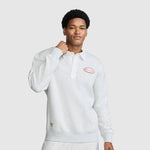 A man stands against a plain gray background wearing the Champion Fleece Rugby shirt in light gray, distinguished by its collar and a small red Champion logo on the chest. This athletic fleece top blends classic rugby shirt styling with modern comfort, as he lifts one hand to his collar.