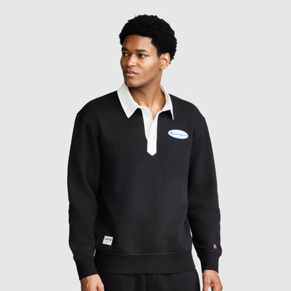 A man wearing the Champion Fleece Rugby shirt in black, featuring a white collar and a small Champion logo on the chest, stands against a plain gray background.