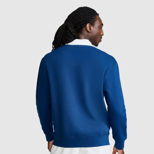 A person with long, dark hair in dreadlocks is shown from the back, wearing the Champion Fleece Rugby shirt in blue layered over a white shirt against a light gray background.