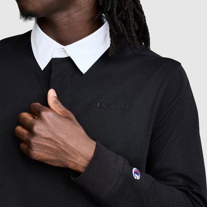 A person in a black Champion Long Sleeve Rugby Shirt with Twill Collar, featuring the embroidered C logo on the chest and sleeve, gives a thumbs up. The shirt’s white collar stands out, and the person’s face is partially out of frame.