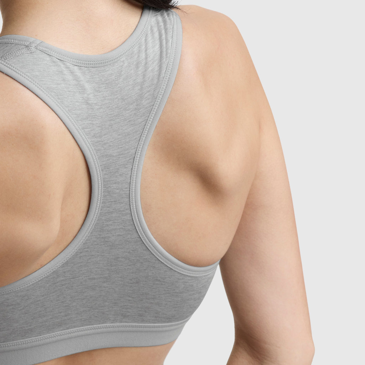 Close-up of a woman’s upper back and shoulder in the Champion Compression Sports Bra, C Logo, light gray. Moderate support and moisture-wicking fabric keep you comfortable during workouts against a plain background.