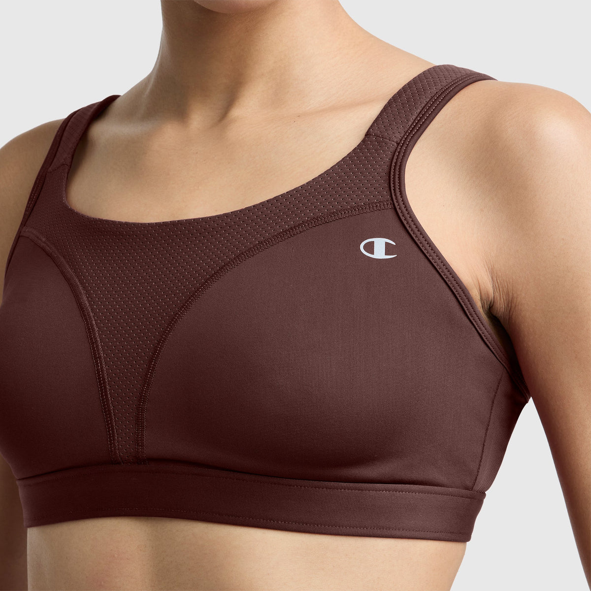 A person wearing a maroon Champion Spot Comfort High-Impact Sports Bra with the C logo, shown from the shoulders to the mid-torso against a neutral background.