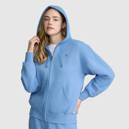 A woman wearing the Champion Powerblend Fleece Zip-Up Hoodie, C Logo, with the hood up and paired with matching sweatpants, stands against a plain light gray background.