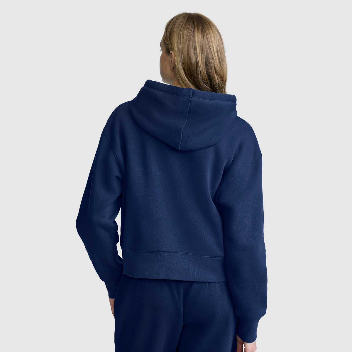 A person with light brown hair is shown from the back, wearing a navy blue Champion Cropped Zip-Up Hoodie and matching pants, standing against a plain light gray background.