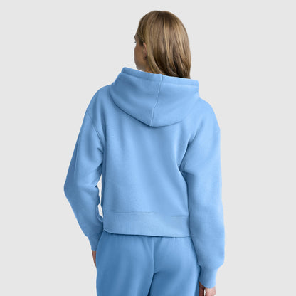 A person with light brown hair stands facing away, wearing a light blue Champion Cropped Zip-Up Hoodie and matching sweatpants against a plain light gray background.