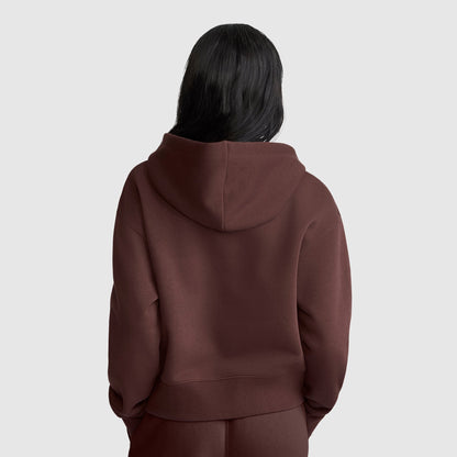 A person with long dark hair is wearing a brown Champion Cropped Zip-Up Hoodie and matching pants, standing with their back facing the camera against a plain light gray background.