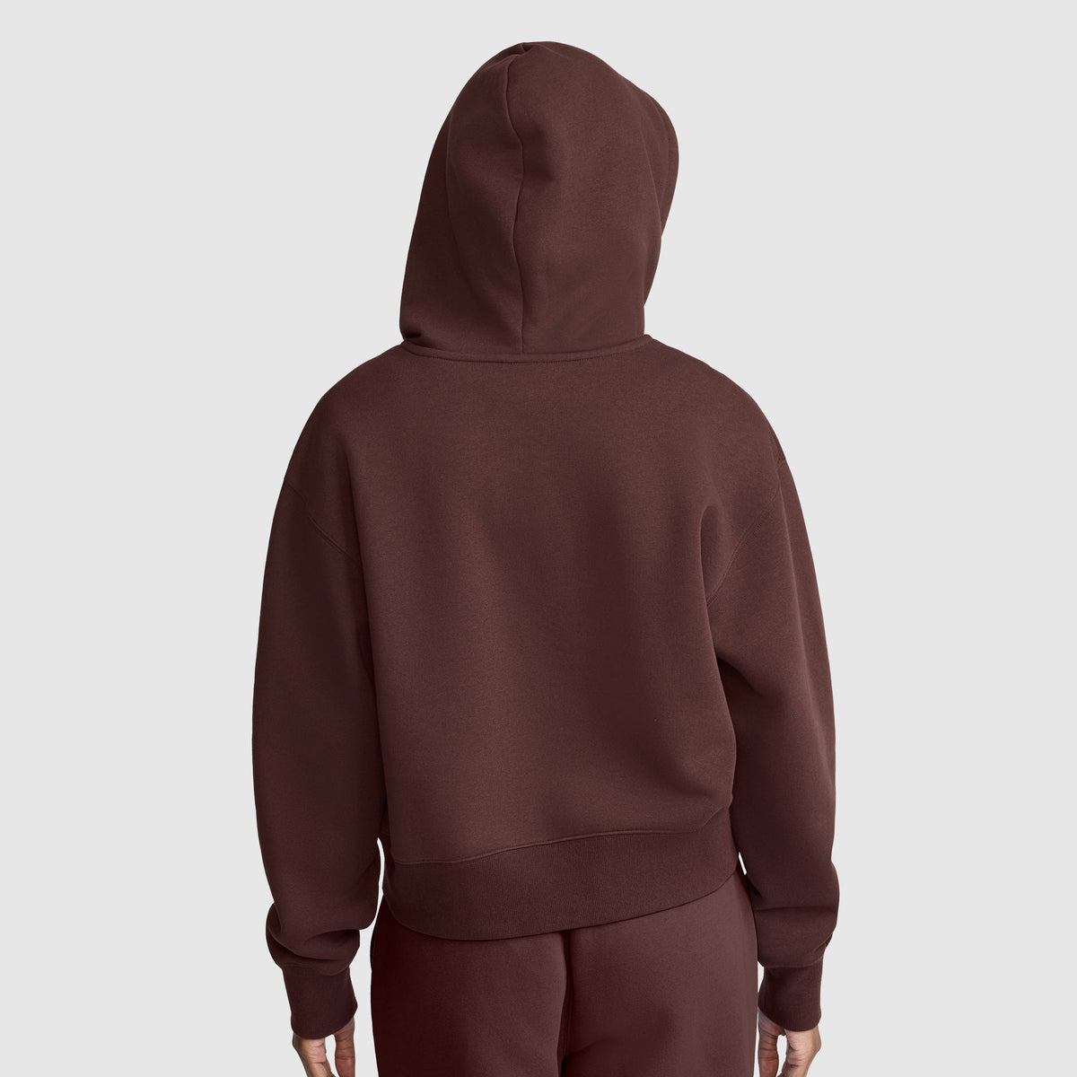 A person wearing a brown Champion Cropped Zip-Up Hoodie and matching pants stands facing away from the camera against a plain light gray background.