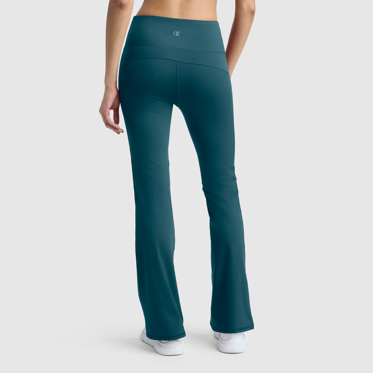 A person is shown from the back, standing against a plain light gray background, wearing Champion Soft Touch Flare Leggings with anti-odor technology and a C logo in teal, paired with white sneakers.