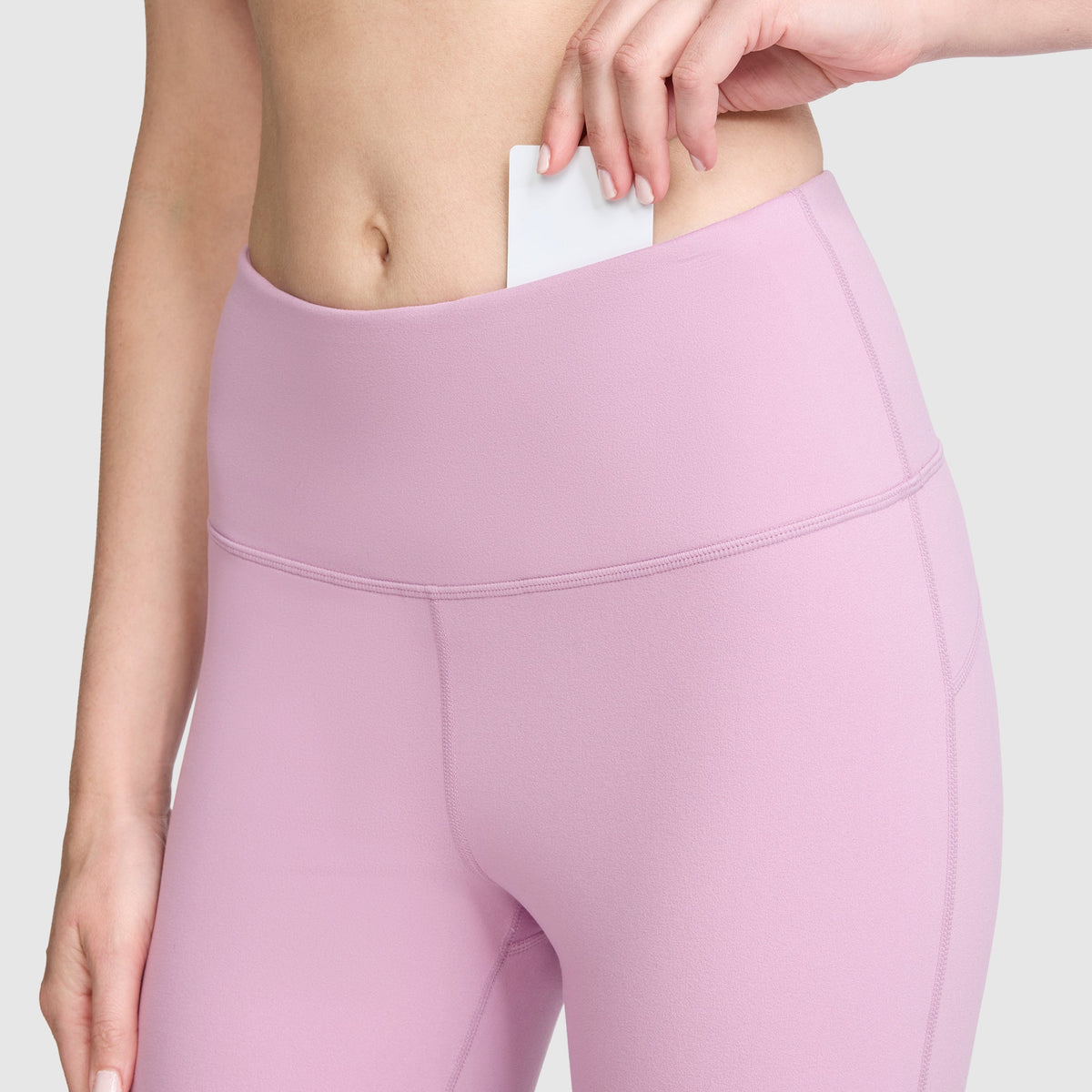 A person wearing Champion Soft Touch Flare Leggings with the C Logo, featuring anti-odor technology, slips a white card into the waistband pocket, with the focus on their hand and midsection.