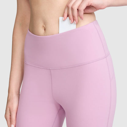 A person wearing Champion Soft Touch Flare Leggings with the C Logo, featuring anti-odor technology, slips a white card into the waistband pocket, with the focus on their hand and midsection.