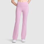 A person wearing Champion Soft Touch Flare Leggings (Anti Odor, C Logo) in high-waisted light pink—perfect workout leggings for women—and white sneakers stands against a plain light gray background, with their hands behind their back.