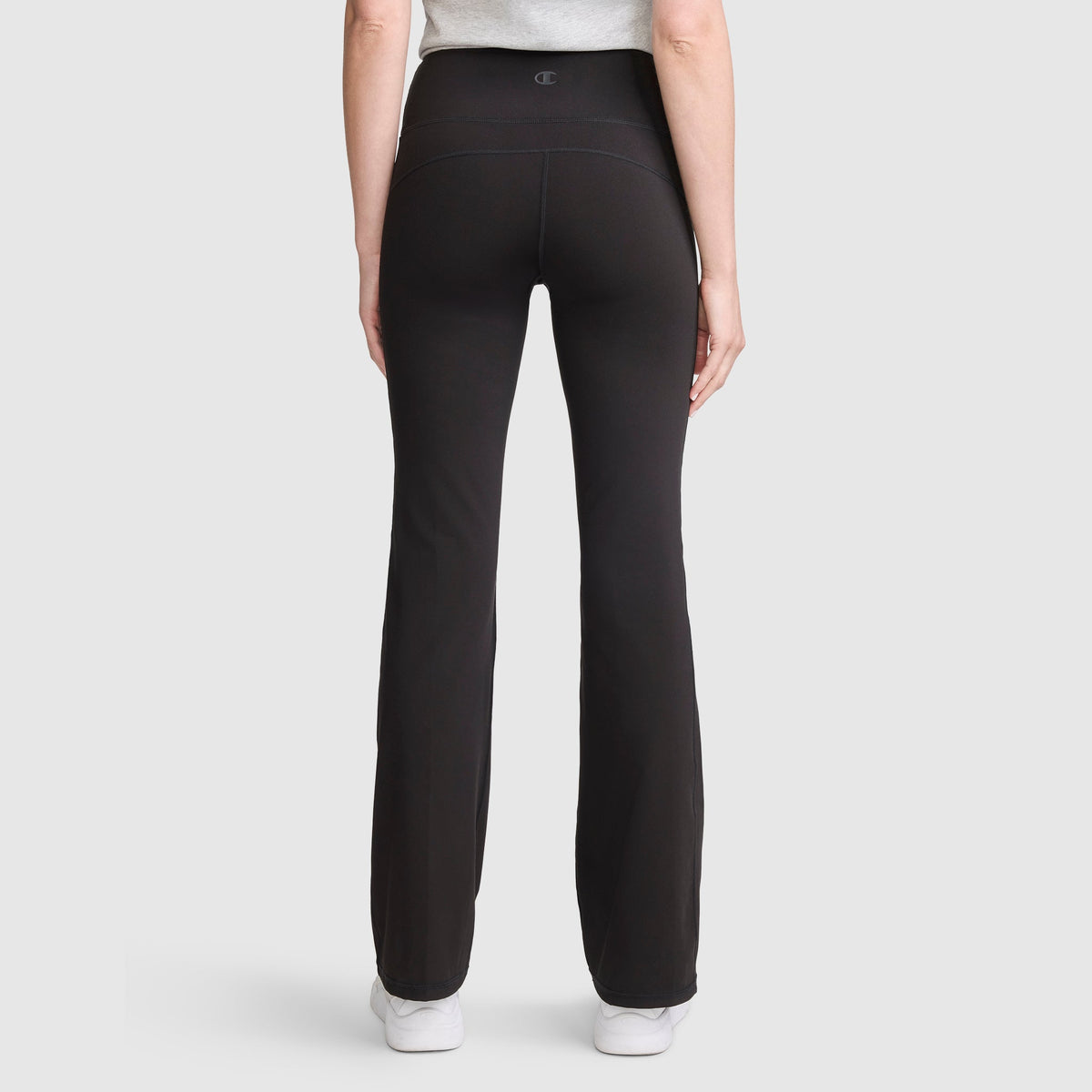 A person is seen from the back wearing Champion’s Soft Touch Flare Leggings with anti-odor technology and C Logo in black, paired with a light gray top, standing against a plain light background.