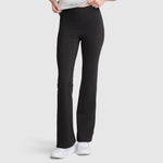 A person wearing Champion Soft Touch Flare Leggings with anti-odor technology and C logo in black, paired with white sneakers, stands against a plain light gray background. The upper body is partially visible, and their hands are adjusting the waistband of these workout leggings for women.