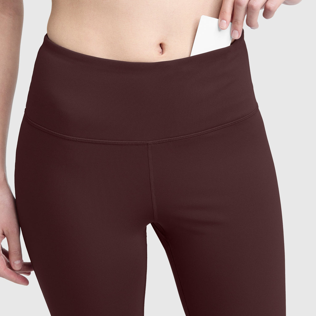 A person slips a card into the discreet waistband pocket of Champion Soft Touch Flare Leggings, featuring anti-odor technology and a signature C logo, highlighting the pocket’s functionality. The image centers on the midsection, keeping the person’s face out of view.