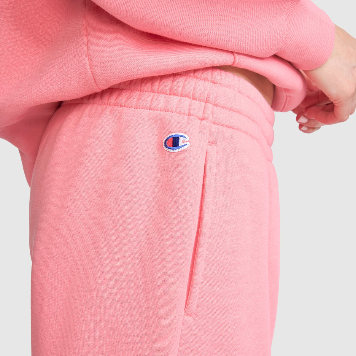 A person is shown from the side wearing Champion’s Powerblend Oversized Sweatpants with the signature C Logo, paired with a matching sweatshirt. Crafted from soft Powerblend fleece fabric, these sweatpants feature the Champion logo above the pocket. The hand rests near the waistband of the oversized fit, set against a plain, light-colored background.