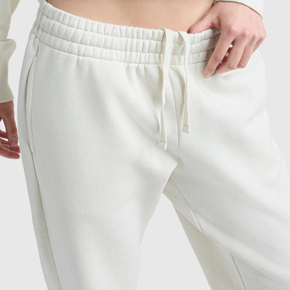 A close-up of a person wearing Champion Powerblend Oversized Sweatpants with C Logo, featuring an elastic waistband and drawstring. One hand rests on the waist, highlighting this cozy loungewear against a plain, light background.
