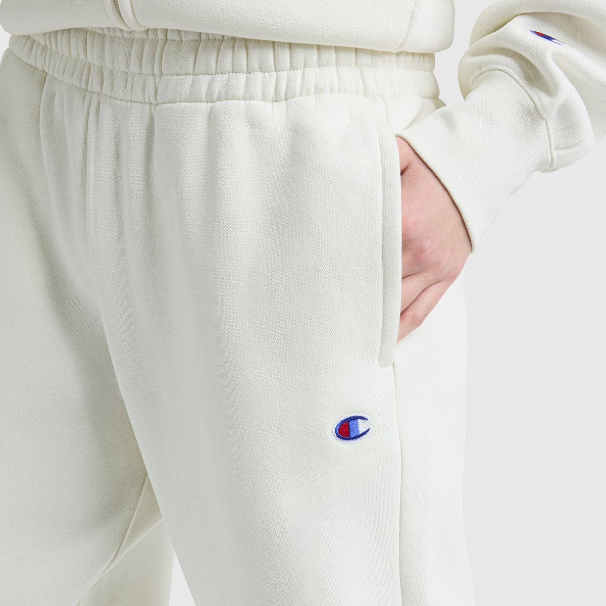 A person wearing Champion's Powerblend Oversized Sweatpants, C Logo, in cream with a matching sweatshirt and one hand in their pocket—comfortably styled women's loungewear ideal for relaxing days.