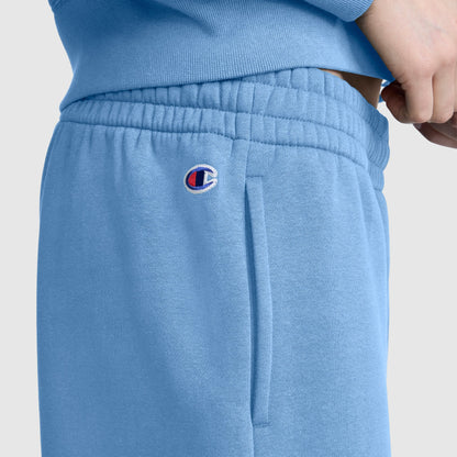 Wearing Champion’s Powerblend Oversized Sweatpants, C Logo in light blue, a person pairs the cozy fleece pants with a matching sweatshirt. The small Champion C logo is embroidered near the pocket, and their hand rests casually at the waistband, showcasing both comfort and style.