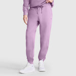A person wears Champion Powerblend Joggers, C Logo in lavender with a matching sweatshirt and white athletic shoes, standing against a plain light background. Only the lower body and part of one arm are visible—perfect for showcasing your favorite Champion women's joggers in a relaxed yet stylish way.