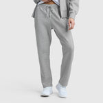 A person stands against a plain light background, shown from the shoulders down, wearing Champion Powerblend Straight Hem Sweatpants in light gray fleece with a matching zip-up hoodie and white sneakers.