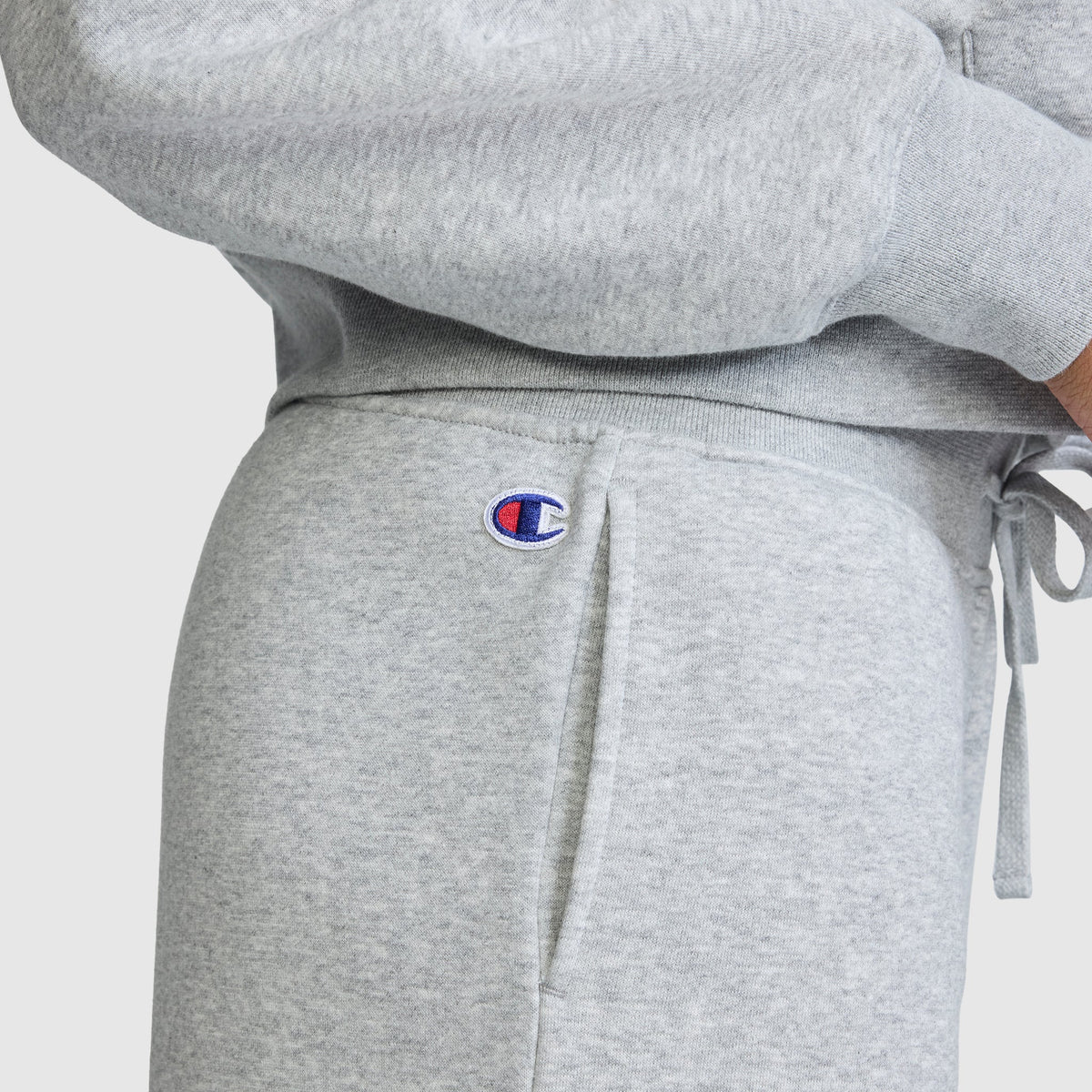 A person is wearing light gray Champion Wide Leg Fleece Sweatpants, featuring the signature C Logo near the pocket, paired with a matching sweatshirt. The comfortable and casual outfit is perfect for lounging in cozy women’s fleece sweatpants from Champion.