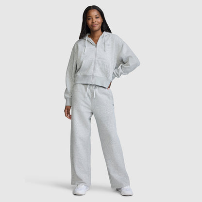 A woman stands confidently in a light gray zip-up hoodie and matching Champion Wide Leg Fleece Sweatpants, C Logo, paired with white sneakers against a simple light background—a sleek ensemble ideal for modern women's loungewear.