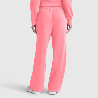 A person is seen from the back wearing bright pink Champion Wide Leg Fleece Sweatpants with a C Logo, paired with a matching sweatshirt. The sweatpants have a loose fit and straight-leg cut, similar to wide leg styles. The outfit is completed with white sneakers.