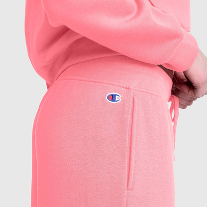 Close-up of a person wearing Champion Wide Leg Fleece Sweatpants, C Logo, in light pink. The embroidered Champion C logo is visible near the pocket of the pants. The wide leg fleece design creates a relaxed look against the plain light gray background.