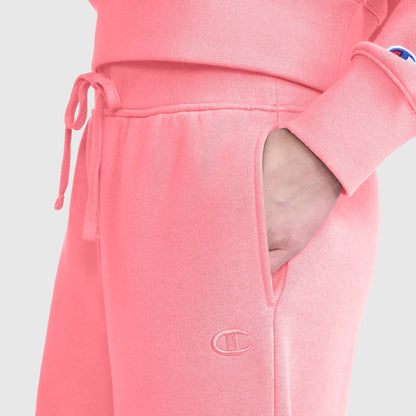 A person is wearing Champion’s Wide Leg Fleece Sweatpants, C Logo, and a matching pink sweatshirt with their right hand in the pocket. The Champion logo is visible on both the sweatpants and the sweatshirt sleeve. The background is plain light gray.