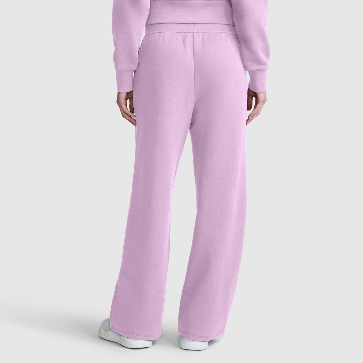 A person is shown from the back wearing Champion’s Wide Leg Fleece Sweatpants with C Logo in light purple, paired with a matching sweatshirt and white sneakers, set against a plain light gray background.