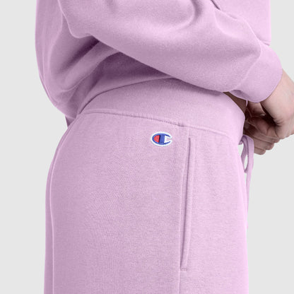 A person is wearing Champion's Wide Leg Fleece Sweatpants, C Logo, in light purple with the Champion logo visible near the waistband, paired with a matching sweatshirt and standing with hands clasped.