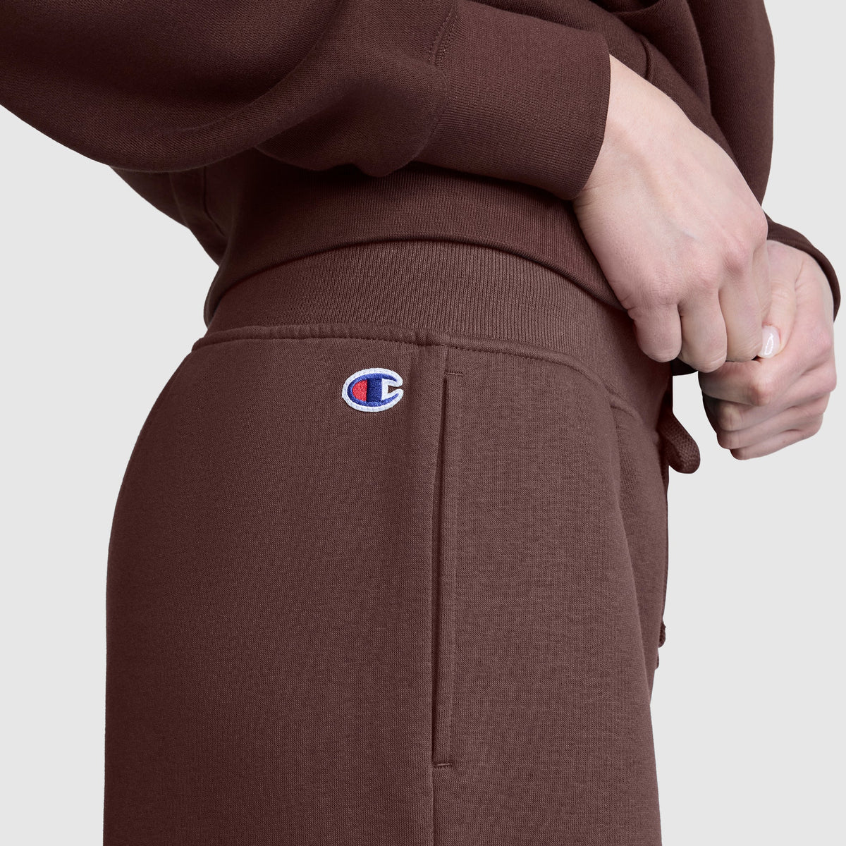 A person is wearing brown Champion Wide Leg Fleece Sweatpants, featuring the C Logo, paired with a matching brown sweatshirt. With hands resting near the waistband, only the torso and upper legs are visible, highlighting the comfort of these women’s cotton fleece pants by Champion.