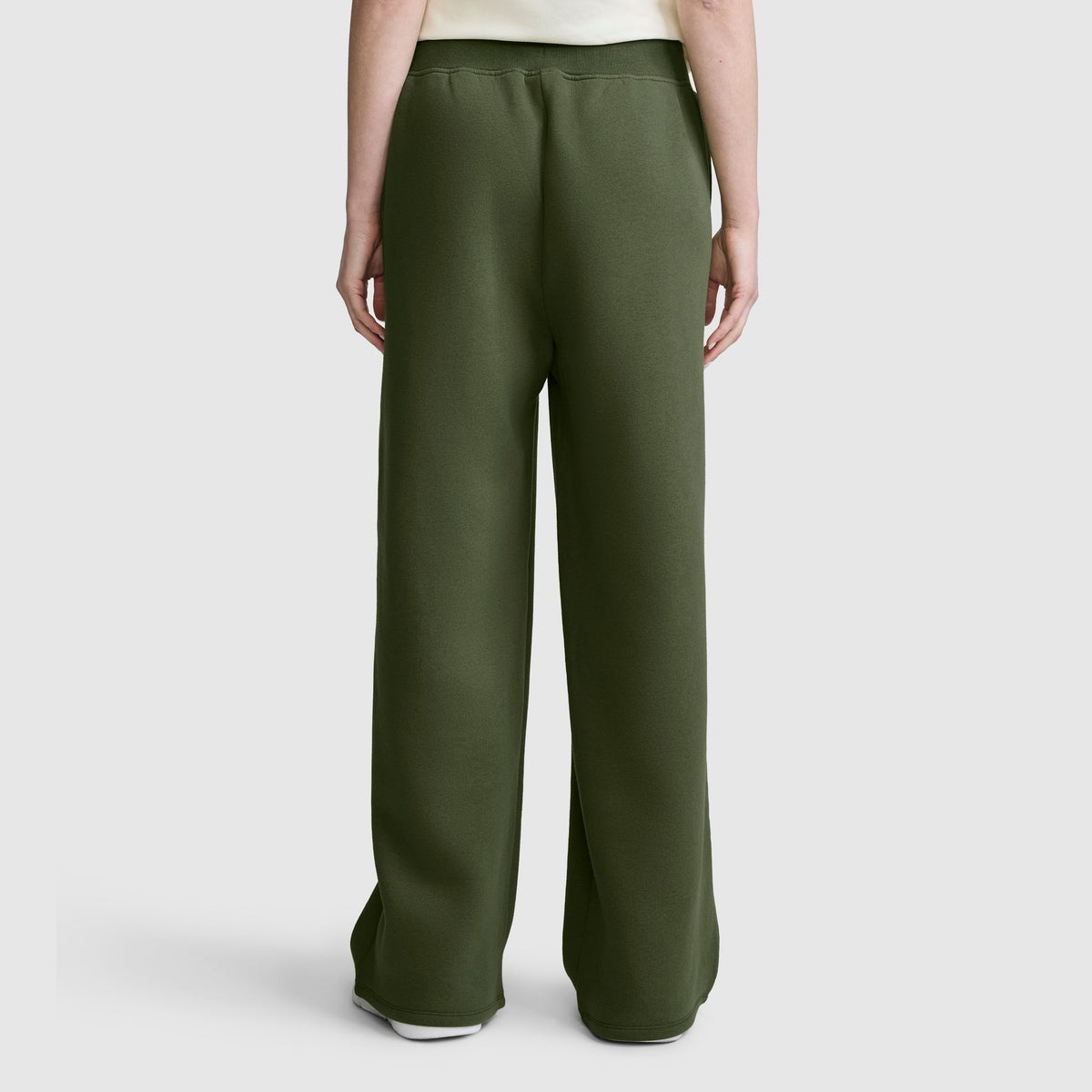 A person is shown from the back, standing against a plain light gray background, wearing the Champion Wide Leg Fleece Sweatpants with C Logo in dark green and a white shirt.
