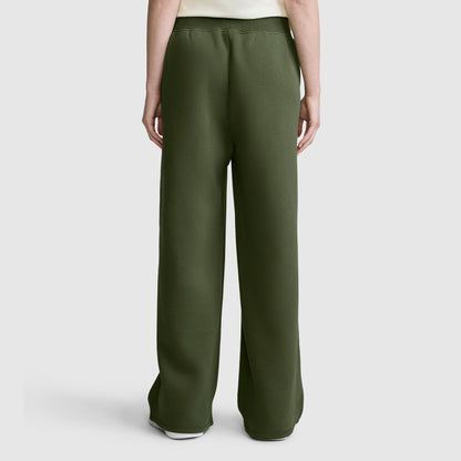 A person is shown from the back, standing against a plain light gray background, wearing the Champion Wide Leg Fleece Sweatpants with C Logo in dark green and a white shirt.