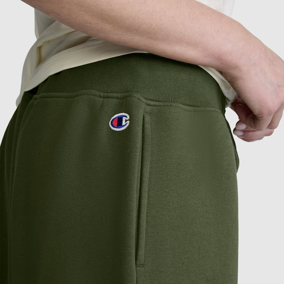 A person wears Champion Wide Leg Fleece Sweatpants with a C logo near the pocket, paired with a light-colored shirt.