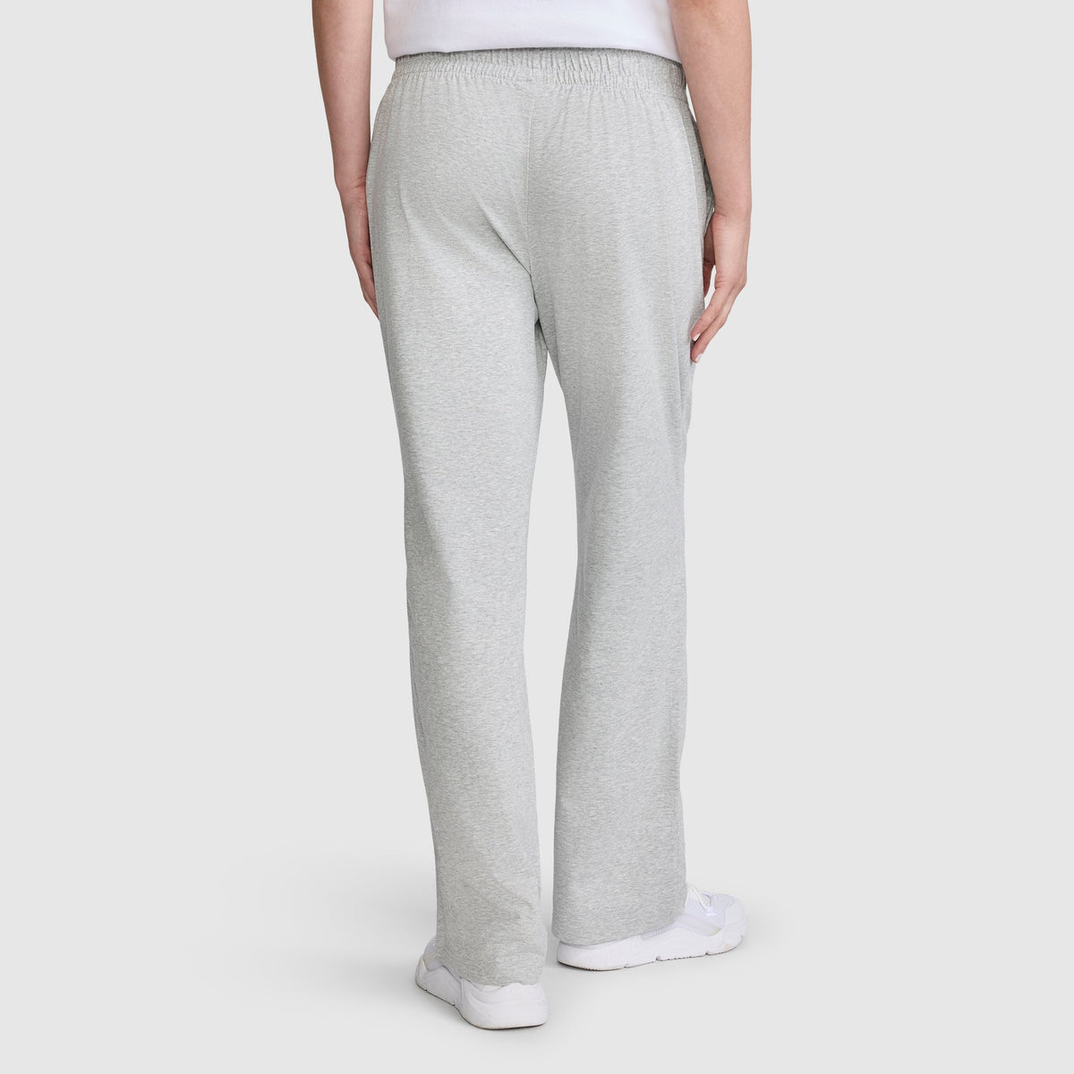 A person wearing Champion Lightweight Lounge Pants, C Logo in light gray jersey cotton and white sneakers is shown from the back, standing against a plain white background. These pants offer superior comfort and style with Champion quality craftsmanship.