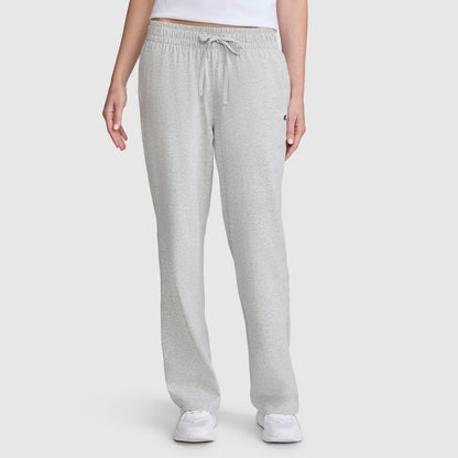 A person wearing Champion Lightweight Lounge Pants, C Logo in light gray, along with a white shirt and white sneakers, stands against a plain white background. Only the lower torso and legs are visible.